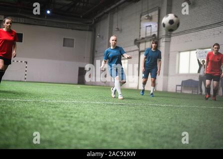 Junge weibliche footbal Spieler in Blau und Rot Sport einheitliche bei Soccer Ball in Richtung Tor suchen während des Spiels Stockfoto