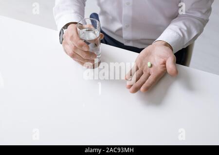 Elegante Geschäftsmann in weißem Hemd holding Glas Wasser und Schmerzmittel während der Sitzung von Schreibtisch und Pille zu nehmen Stockfoto
