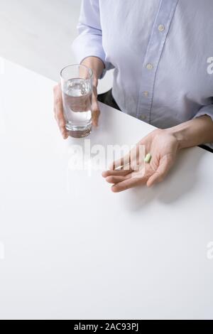 Hände von Kranken weiblich oder Geschäftsfrau im Hemd, Glas Wasser und Pille zu haben, Sitzen, Schreibtisch Stockfoto