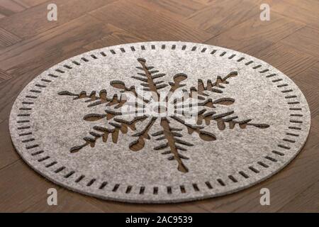 Ein hellgrauer Filz runde Teller mat in Form eines Flocke Schnee lag auf einem dunklen Holztisch Stockfoto