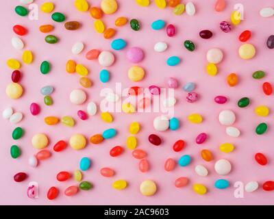Viele verstreute bunte Süßigkeiten, Bonbons, Lutscher auf einem hellen rosa Hintergrund, Ansicht von oben Stockfoto