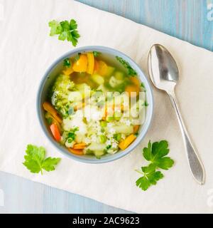 Helle Frühling pflanzliche Ernährung vegetarische Suppe mit Blumenkohl, Brokkoli, Paprika, Karotten, Erbsen, Nudeln, Petersilie. Ansicht von oben, blauen Hintergrund. Stockfoto