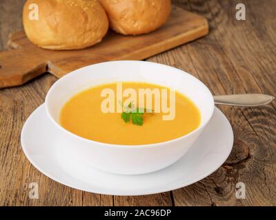 Weiße Schüssel Kürbiscremesuppe, garniert mit Petersilie auf Holz- Hintergrund, Seitenansicht. Stockfoto