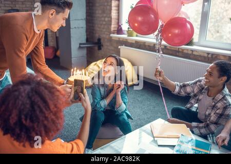Freund gratulieren. Schöner Freund mit seiner Freundin Geburtstag zu gratulieren bringt Kuchen mit Kerzen Stockfoto