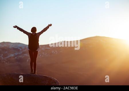 Glückliches Mädchen steht mit erhobenen Armen gegen Sonnenuntergang Licht Stockfoto