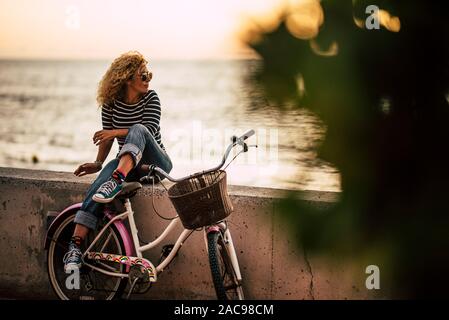 Nach kaukasische Frau genießen outdor Freizeit entspannen Sie sich nach einem Ritt auf einem vintage Bike, sitzen auf einer Mauer am Meer - gesund aktiv Stockfoto