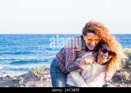 Paar nach Nizza kaukasischen Frauen spielen sie zusammen, die sich gegenseitig mit viel Spaß und Lachen - Menschen lachen im Outdoor Freizeit - Ozean Stockfoto