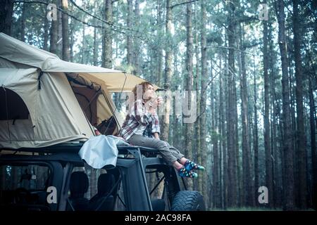 Glücklich sich schöne Menschen kaukasischen Frau sitzen auf dem Dach des Autos mit Zelt auf ihn für freies Reisen camping Lebensstil - wanderlust Veh montiert Stockfoto