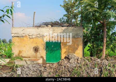 Aufgegeben exotische Gelb geschaukelt Hütte mit einzigen grünen Holz- grunge Tür, tropischen grünen Bäumen und viel Lehm am Dorf an einem sonnigen Tag Stockfoto