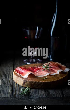Italienische Prosciutto Crudo oder jamon mit Rosmarin auf dunklem Hintergrund. Rohen Schinken. Stockfoto