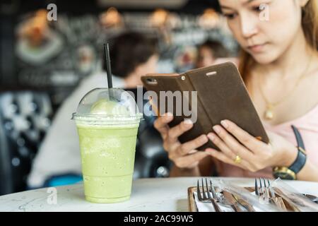 Frau mit Smart Phone, Foto, grüner Tee frappe im Cafe Stockfoto