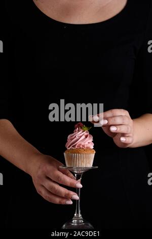 Schöne und duftende Cupcake mit Himbeer Creme und einem Zweig Minze, Hände von einem Koch auf schwarzem Hintergrund Stockfoto