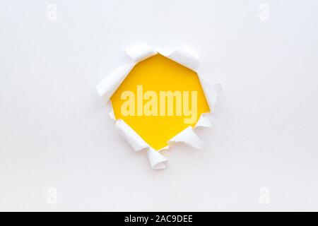 Ein rundes Loch in weißem Papier mit zerrissene Kanten mit einer leuchtend gelben Farbe Papier Hintergrund im Inneren. Stockfoto