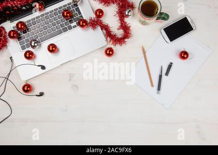 Job bei Weihnachtsferien: Flach aus einem leichten hölzernen Tisch mit einem offenen Aluminium Laptop, rote Dekoration, rote Kugeln, Weihnachten Tasse Tee, smartphon Stockfoto