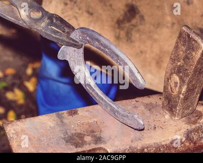 Schmied am Amboß, ein Hufeisen. Traditionelle Werkzeuge für das Handwerk in der Werkstatt. Schmied beruf Konzept. Stockfoto