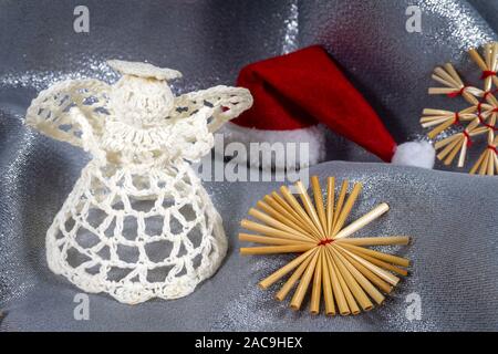 Handgefertigte gestricken Weihnachten Engel Dekoration mit natürlichem Stroh Schneeflocken auf einer zerdrückten Silber Stoff mit Kopie Raum Stockfoto