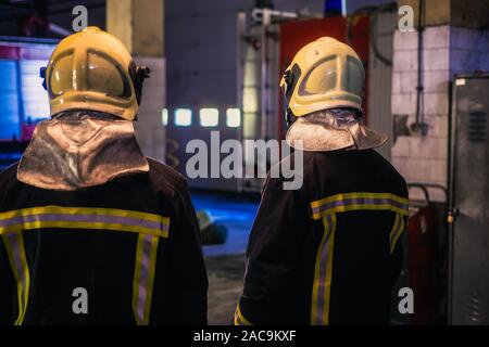 Zwei junge Männer mit Helm von der Rückseite in der Feuerwache posieren. Stockfoto