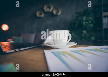 7/8 Nahaufnahme foto Tasse Kaffee fertig getrunken auf Platte in der Nähe von Diagramm arbeit Papier und Laptop auf der rechten Seite. Stockfoto