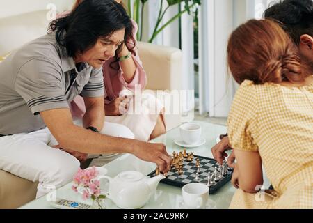Im mittleren Alter paar Schach spielen mit ihren erwachsenen Kindern und Tee trinken. Stockfoto