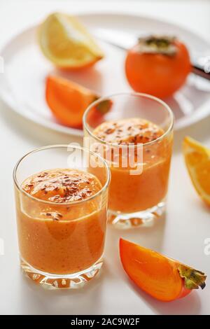 Zwei Gläser von kakipflaume Smoothies mit Leinsamen. Im Hintergrund Schichten von kakipflaume und orange. Stockfoto