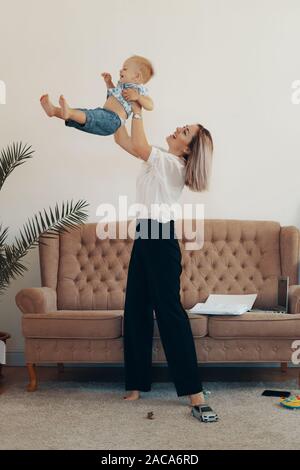 Junge Mutter mit ihrem Kind zu Hause arbeiten. Business Mamma eine Auszeit nimmt. Multitasking, freiberufliche und Mutterschaft Konzept Stockfoto