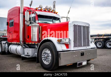 Leistungsstarke hell rot Classic Big Rig Semi Truck Traktor mit Chrom Zubehör und Signalhörner auf dem Dach und Flachbett Auflieger auf Ware Stockfoto