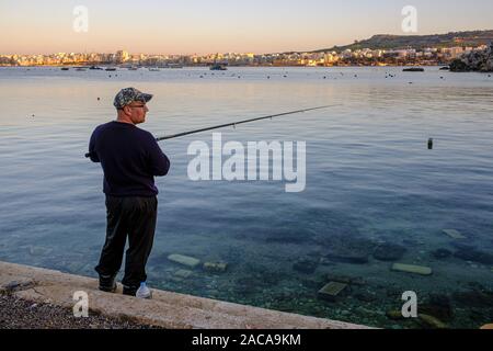 Angeln am Abend bei Mistra Bay mit Blick auf Saint Paul's Bay in Bugibba, Malta Stockfoto