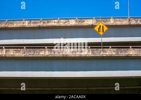 Warnung Verkehr Schild zeigt eine Verengung der Straße auf einer der Ebenen eines mehrstufigen Straße Überführung vor blauem Himmel befindet. Stockfoto