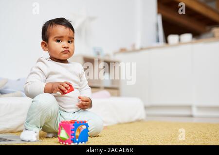Cute afrikanischen Mädchen auf Kamera, während auf dem Boden saß und mit Spielzeug spielen zu Hause Stockfoto