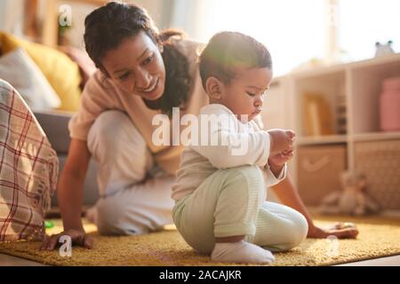 Süße kleine Baby Junge sitzt auf dem Boden und spielt mit seiner Mutter in der Nähe von ihm und mit ihm spielen zu Hause Stockfoto