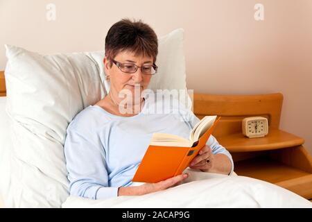 Senioren in einem Pflegeheim mit einem Buch im Bett Stockfoto