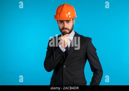 Nachdenkliche junge Ingenieur Kaufmann in Bau Helm. Mann über Ideen und Arbeiten über blauen Hintergrund denken. Stockfoto