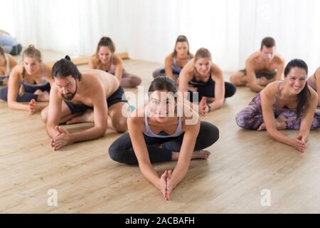 Gruppe von jungen sportlich attraktive Leute im Yoga Studio, Yoga Unterricht mit Kursleiter, sitzend auf dem Boden vorwärts band Stretching yoga Pose