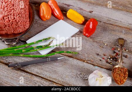 Frisches Rindfleisch Hackfleisch mit Gemüse, bunte Paprika und Spargel, Notebooks, Pen auf alten Holz Hintergrund. Stockfoto