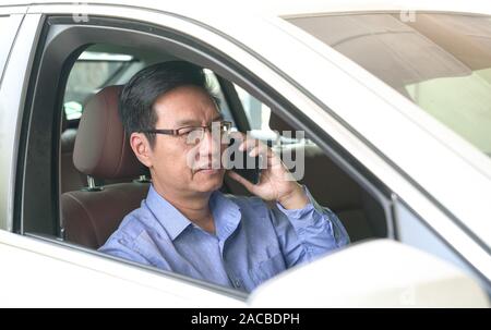 Asiatische chinesischen Geschäftsmann lächelnd und über sein Mobiltelefon in seinem Auto Stockfoto