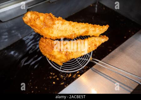 Gekochte und angeschlagene Fische, die in einer Fritteuse in einem Fisch- und Spangeschäft in Großbritannien aus dem Fisch genommen werden Stockfoto