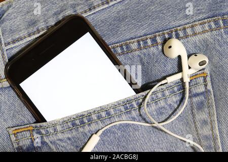 Für Audio- und Videoinhalte Vorlage. Telefon mit einem weißen Bildschirm und Kopfhörer in einer Jeans Tasche. Helle Foto ihr Bild einzufügen. Close Up. Stockfoto