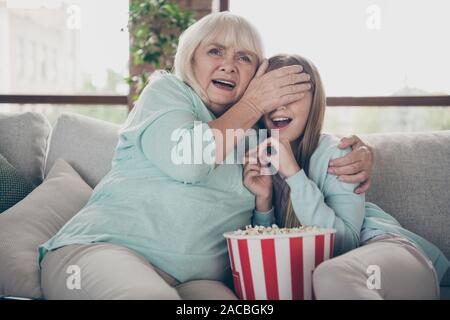 Schauen Sie nicht. Foto von zwei Menschen weiß behaarte Oma kleine Enkelin sitzen Sofa Fernsehen scary Horror Film ausblenden Augen verbringen Wochenende zusammen Stockfoto