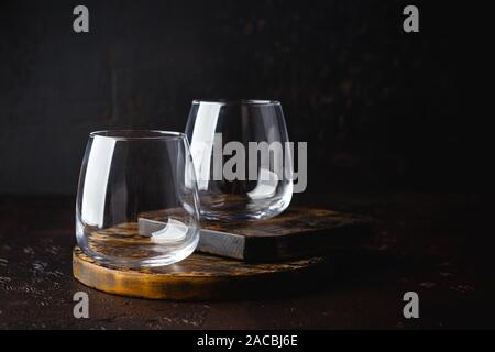 Zwei leere Gläser für Wasser oder Cocktails auf kleinen hölzernen Schneidebrett auf Dunkelbraun Tabelle. Gläser Becher für Getränke. Beverage Konzept Stockfoto
