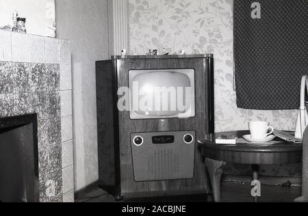 1950, historische, ein Fernseher der Ära in der Ecke eines vorderen Zimmer, England, UK. Aus den frühen bis Mitte der 1950er Jahre, der Fernseher ist in einem auf dem Boden stehende Holz- Shell untergebracht, mit dem Lautsprecher und dails unter dem Bildschirm. Die BBC hatte regelmäßige TV transmssions von Alexander Palace, London 1936 begonnen, aber nicht mehr die Ausstrahlung während WW2, wieder beginnend in 1946. Stockfoto