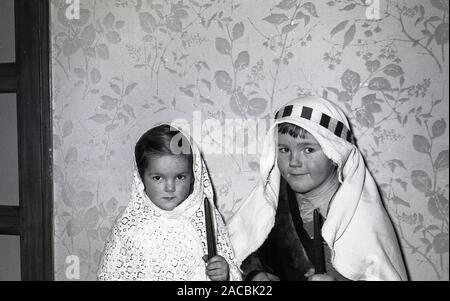 1950, historische, Weihnachten und zwei kleinen Kindern in Krippen Kostüme wie Josef und Maria, die Eltern von Jesus, halten Sie Kerzen, England, UK gekleidet. Stockfoto