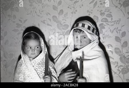 1950, historische, Weihnachten und zwei kleinen Kindern in Krippen Kostüme wie Josef und Maria, die Eltern von Jesus, halten Sie Kerzen, England, UK gekleidet. Stockfoto