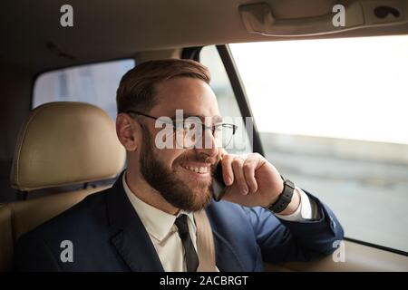 Junge Bartgeier Geschäftsmann in Brillen Gespräch am Handy und lächelnd, während eine Reise im Auto Stockfoto