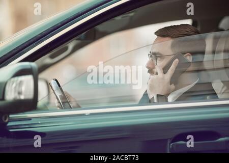 Seitenansicht der jungen Unternehmer in Brillen Gespräch am Handy und gerade für unterwegs im Auto Stockfoto
