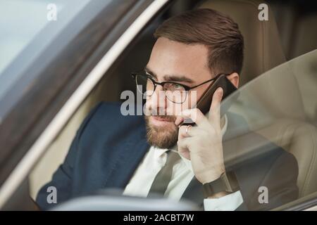 Junge Bartgeier Geschäftsmann in Brillen Gespräch am Handy während der Fahrt Stockfoto