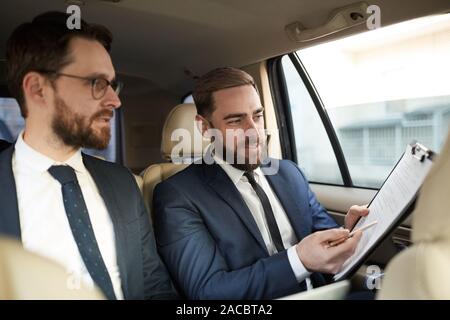 Junge Unternehmer, die an den Vertrag und diskutieren es mit seinem Kollegen, während Sie sitzen auf der Rückbank des Autos Stockfoto