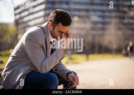 Junge Unternehmer ist sitzt im Park nach abgefeuert wurde. Er ist deprimiert. Stockfoto