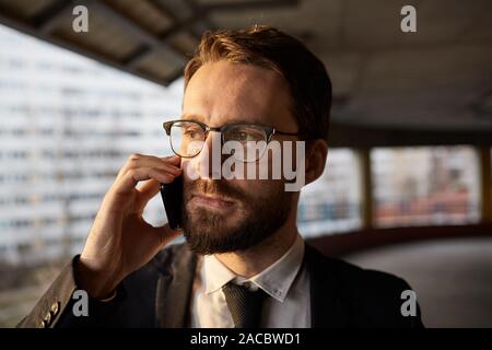 Nahaufnahme der junge Bartgeier Geschäftsmann in Brillen und in der Klage die Konzentration auf sein Gespräch am Telefon im Freien Stockfoto