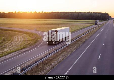 Eine Karawane von modernen Lkw Transporte Fracht am Abend gegen den Sonnenuntergang. Lkws fahren auf der Autobahn am Abend, Logistik Stockfoto