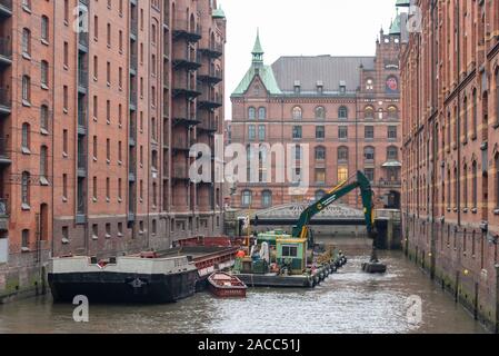 Hamburg, Deutschland. 26 Nov, 2019. Eines Schwimmbaggers holt Schlamm aus einem Kanal in der Speicherstadt. Dies ist die weltweit größte Sammlung von historischen Lagerhäusern, die heute als Bürogebäude, Wohngebäude und Hotels. Die Hamburger Speicherstadt ist ein UNESCO-Weltkulturerbe. Quelle: Stephan Schulz/dpa-Zentralbild/ZB/dpa/Alamy leben Nachrichten Stockfoto